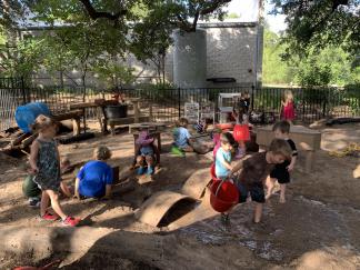 NWPS play yard Young children playing in an outdoor sand and water area with a variety of loose parts.